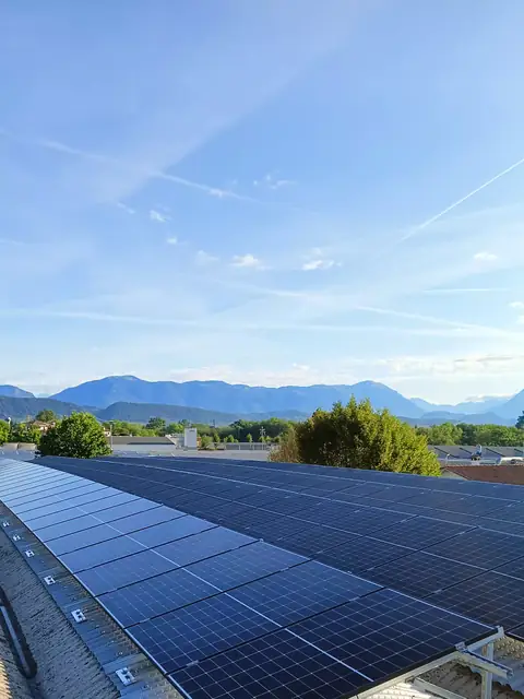 Lunghe file di moduli sulla copertura di un capannone, con le montagne all'orizzonte