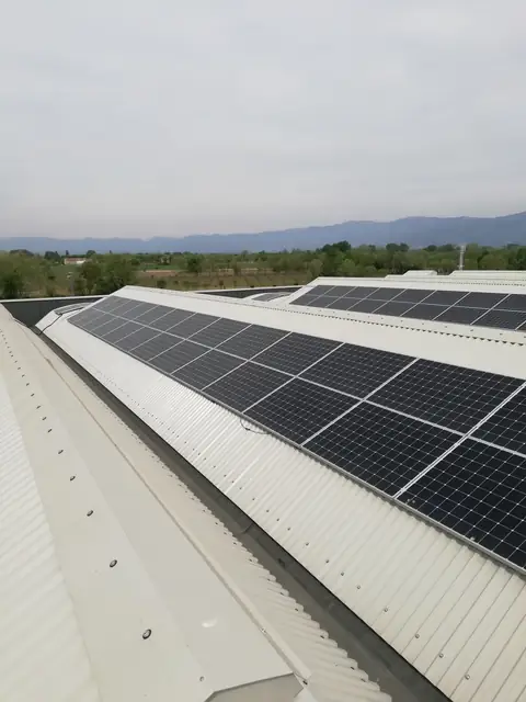 Fila di moduli sulla copertura chiara di un capannone, con la pianura e i monti