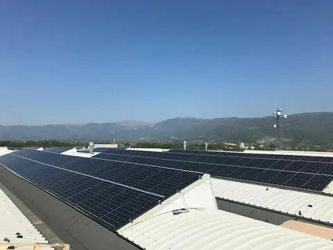 Capannone con le falde coperte di moduli neri e le Prealpi sullo sfondo