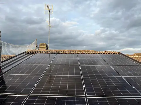 Moduli monocristallini su un tetto in coppi, con l'antenna e la rete anticaduta sotto un cielo nuvoloso