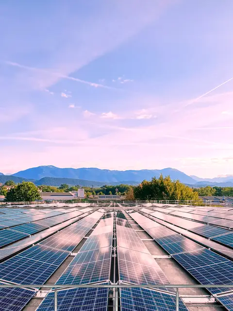 File di moduli su strutture inclinate su un tetto piano al tramonto, con il cielo rosa e le montagne