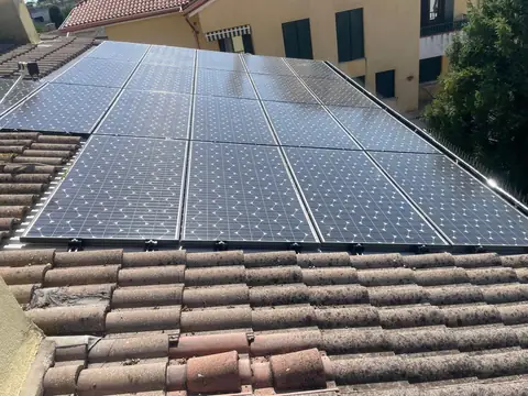 Campo di moduli su un tetto in coppi visto dall'alto, con la casa accanto