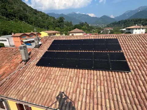 Due file di moduli neri su un tetto in coppi, con il paese e le montagne sullo sfondo