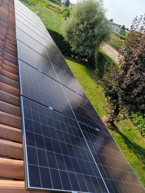 Moduli su un tetto in coppi, sotto il giardino con il prato e la siepe