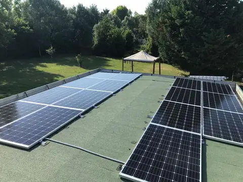 Due file di moduli su un tetto piano con la guaina, sopra un giardino alberato