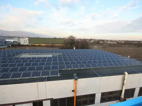 Impianto sul tetto piano di un capannone al tramonto, con la zona industriale e i monti innevati