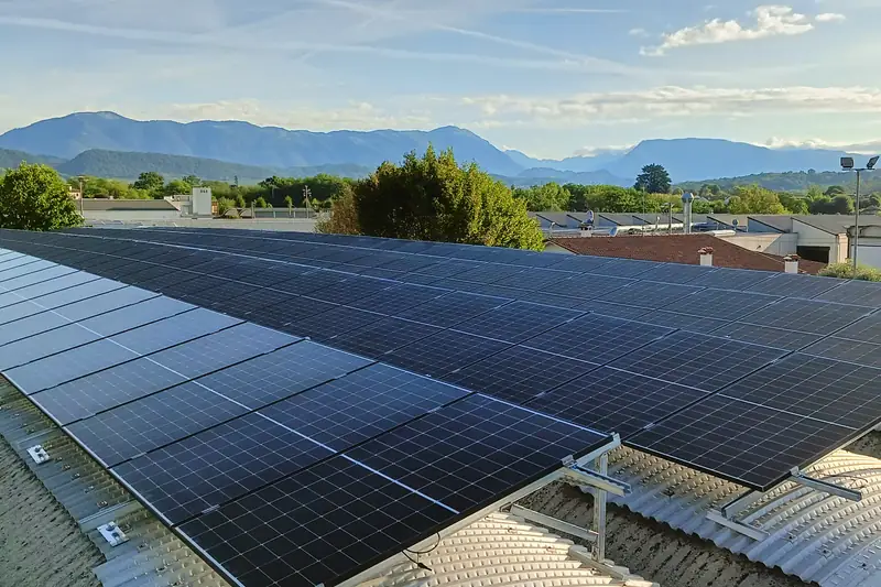 Lunghe file di moduli fotovoltaici sul tetto curvo di un capannone, con le montagne e il cielo del mattino