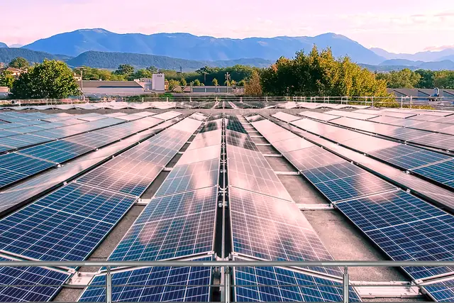File di moduli fotovoltaici su una copertura piana, con le montagne sotto un cielo rosa