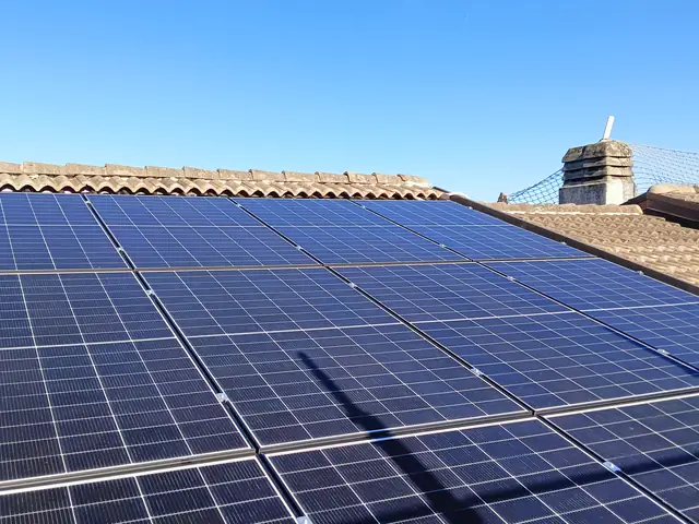 Moduli fotovoltaici su un tetto in tegole sotto un cielo sereno, con un comignolo