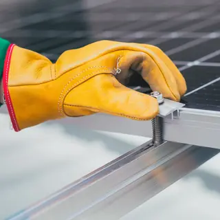Mano con il guanto da lavoro che fissa un morsetto al telaio di un modulo fotovoltaico